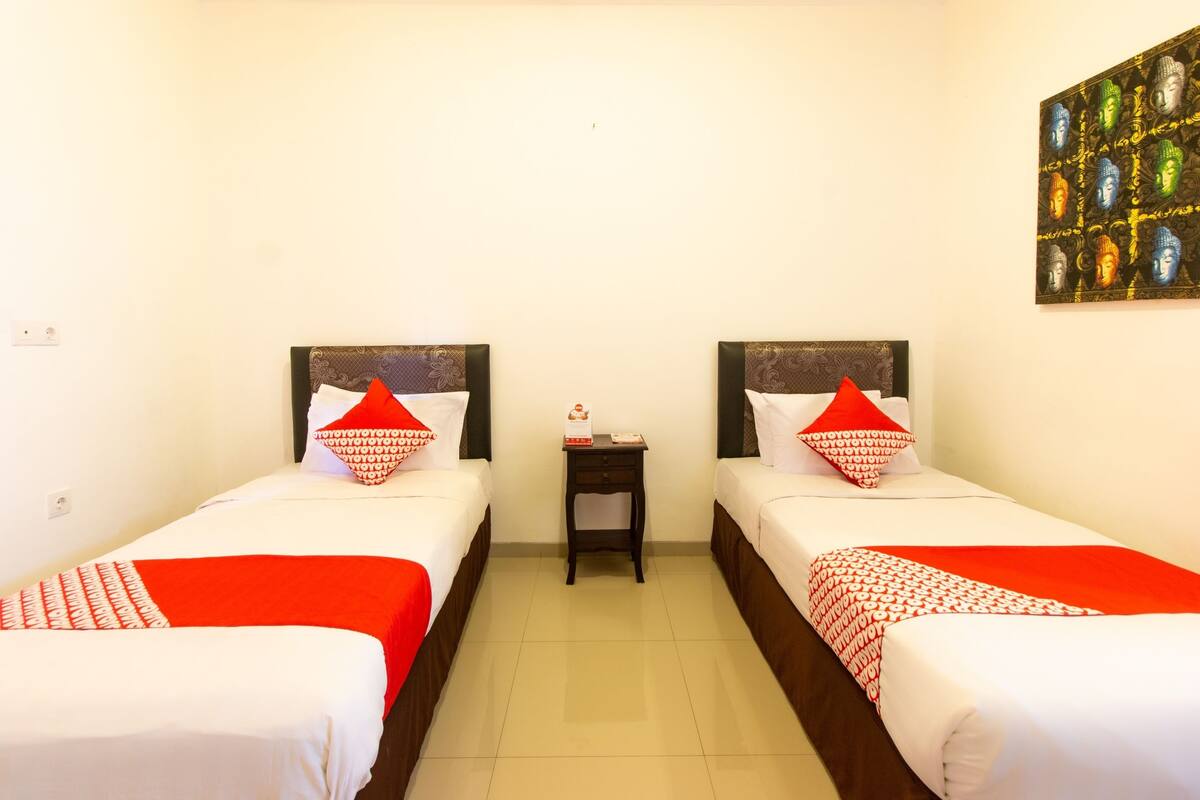 A hotel room with two beds, each with a red and white patterned pillow, a small bedside table, and a wall-mounted artwork.