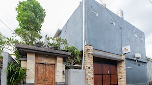 A building with a grey facade, a wooden door, and a stone pillar. - OYO 401 The Frog Homestay Sanur (Denpasar)