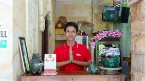 A reception desk with a wooden counter, a framed picture, a small statue, and a vase with flowers. - OYO 401 The Frog Homestay Sanur (Denpasar)