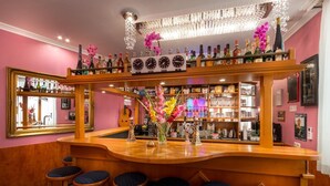 A bar area with a wooden counter, multiple stools, and a variety of bottles and glasses. - Hotel Atlanta Budget (Darmstadt)