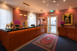 Ein Hotel-Empfangsbereich mit einem Holzbüro, einem roten Teppich und einem Bild an der Wand.