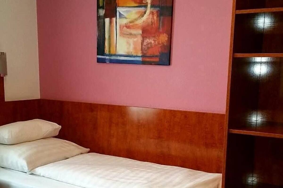 Quarto de hotel com cama de madeira, parede rosa e um quadro sobre a cama.