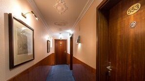 A hallway with a blue carpet, wooden walls, a framed picture, a door with the number 553, and a light fixture on the ceiling. - Hotel Atlanta Budget (Darmstadt)
