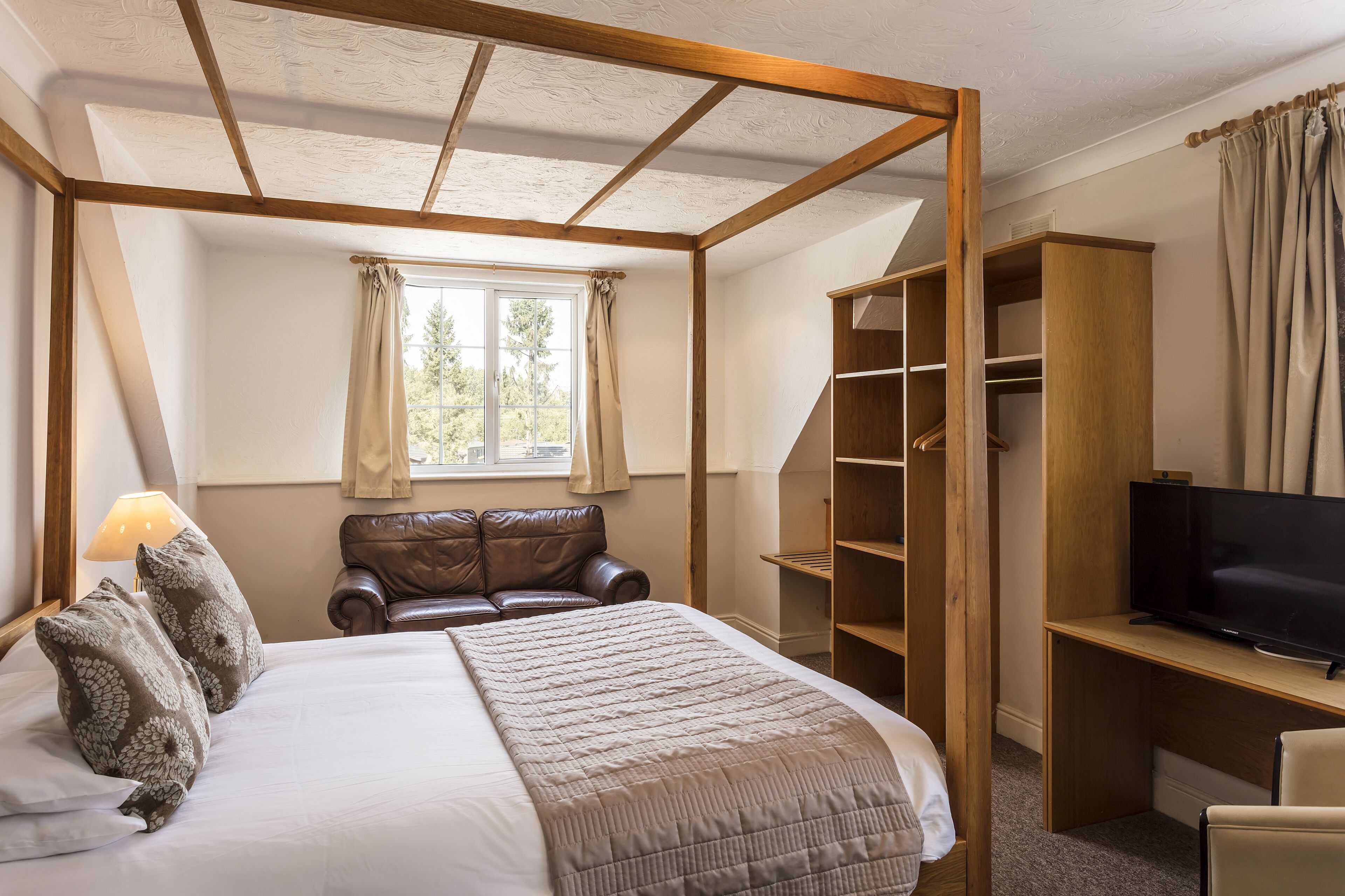 Un dormitorio con una cama con dosel, un televisor sobre un escritorio de madera y un armario.