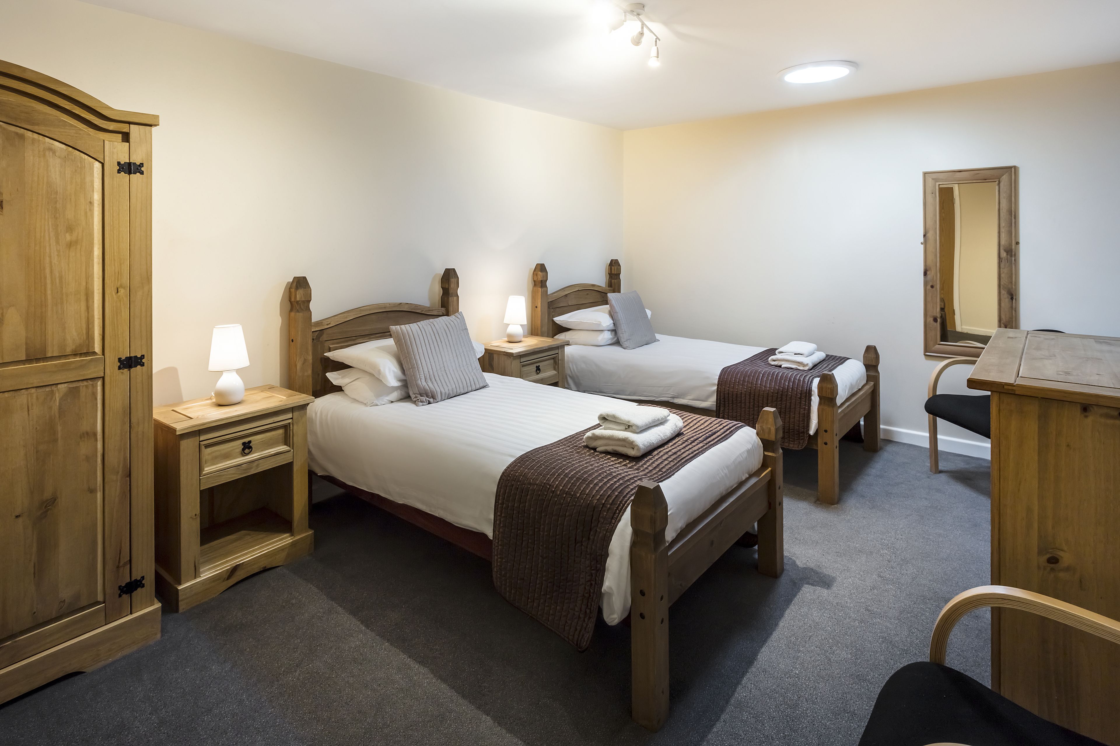 Un dormitorio con dos camas de madera, mesitas de noche, un armario de madera y un espejo.