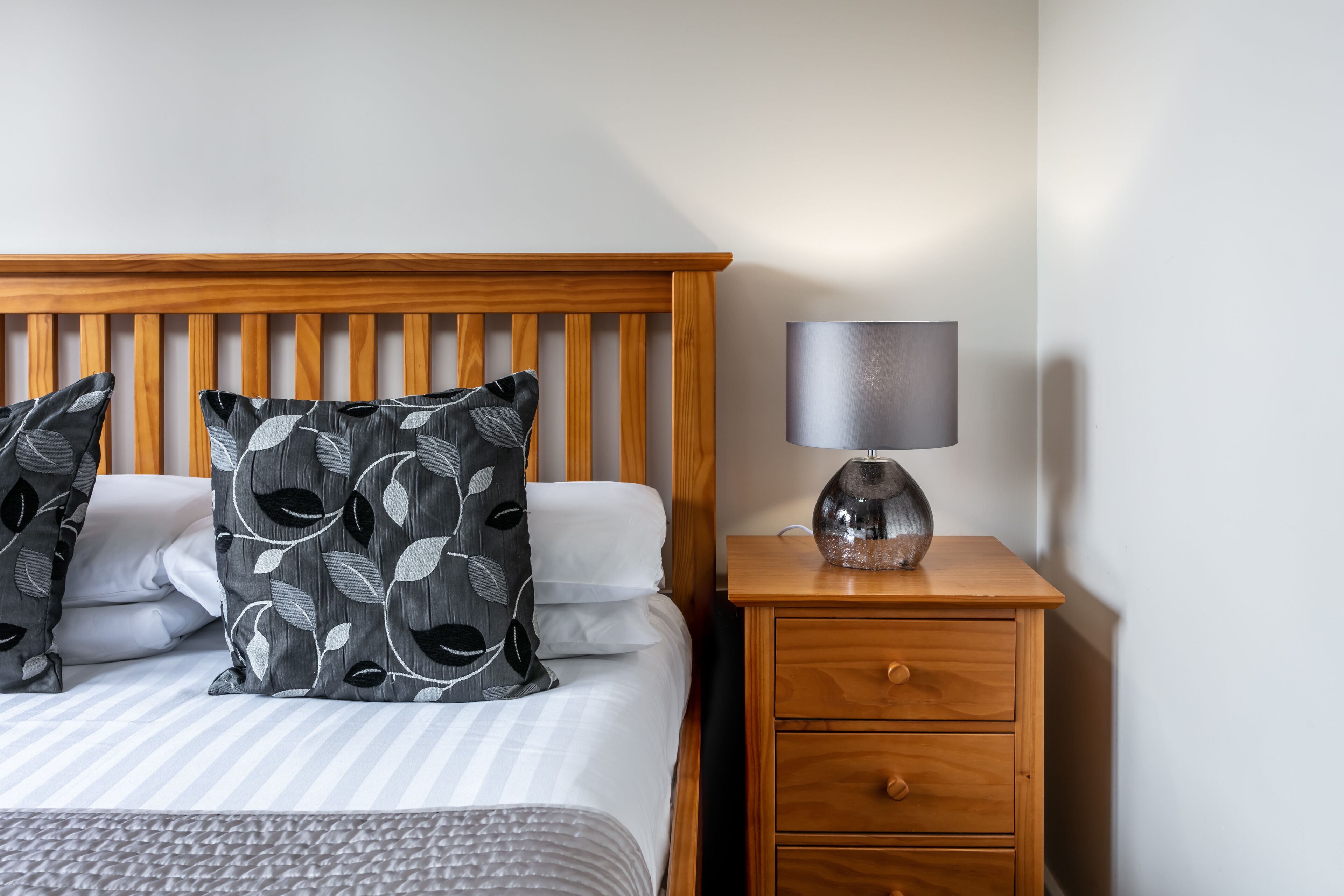 A neatly made bed with patterned pillows, a bedside lamp, and a wooden nightstand with drawers.