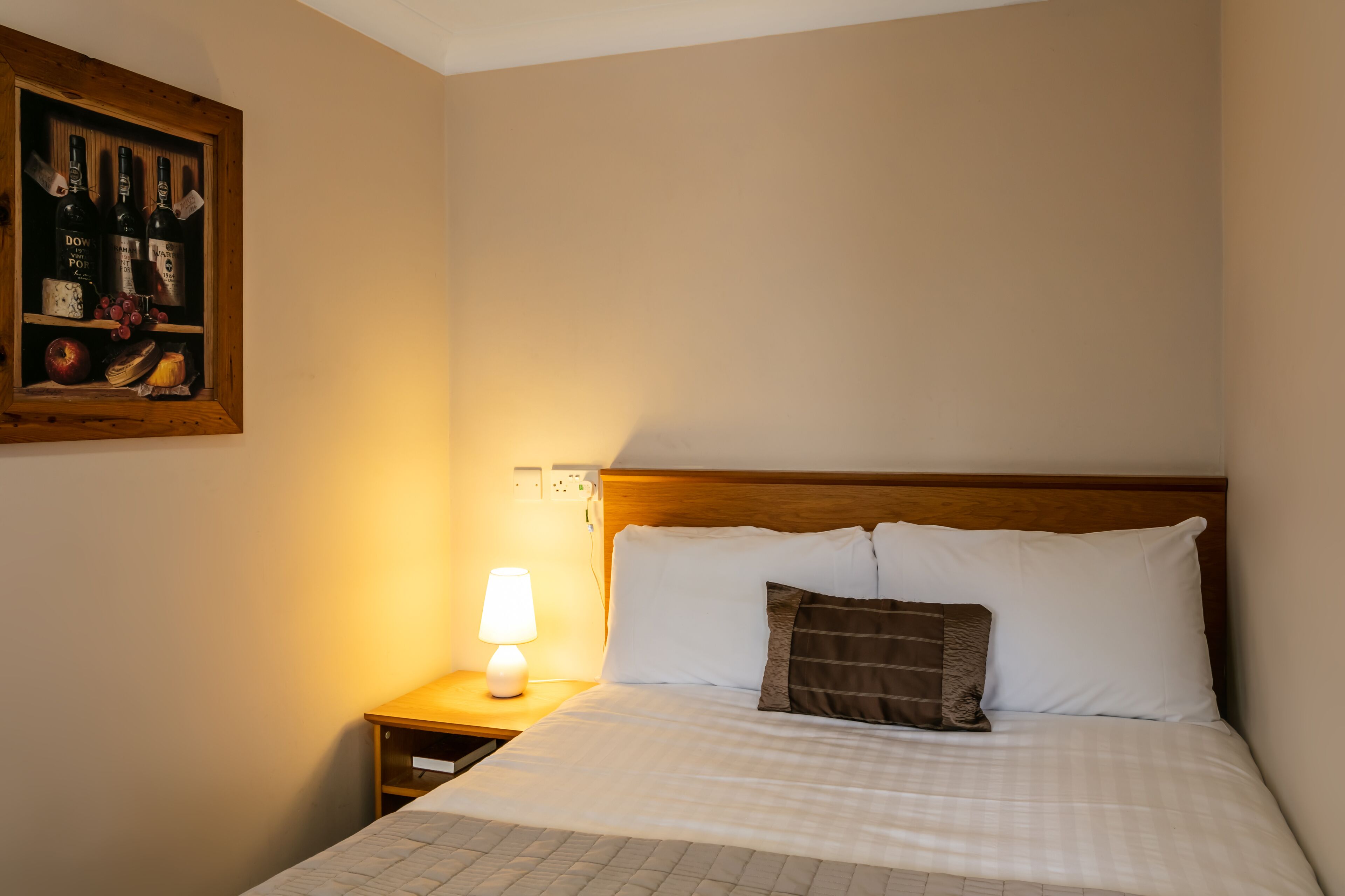 Una habitación de hotel con una cama bien hecha, una lámpara de noche y un cuadro en la pared.