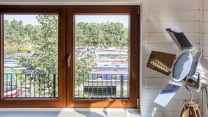 A room with a large window overlooking a marina with boats and a forested area. - Roydon Marina Village Hotel (Harlow)