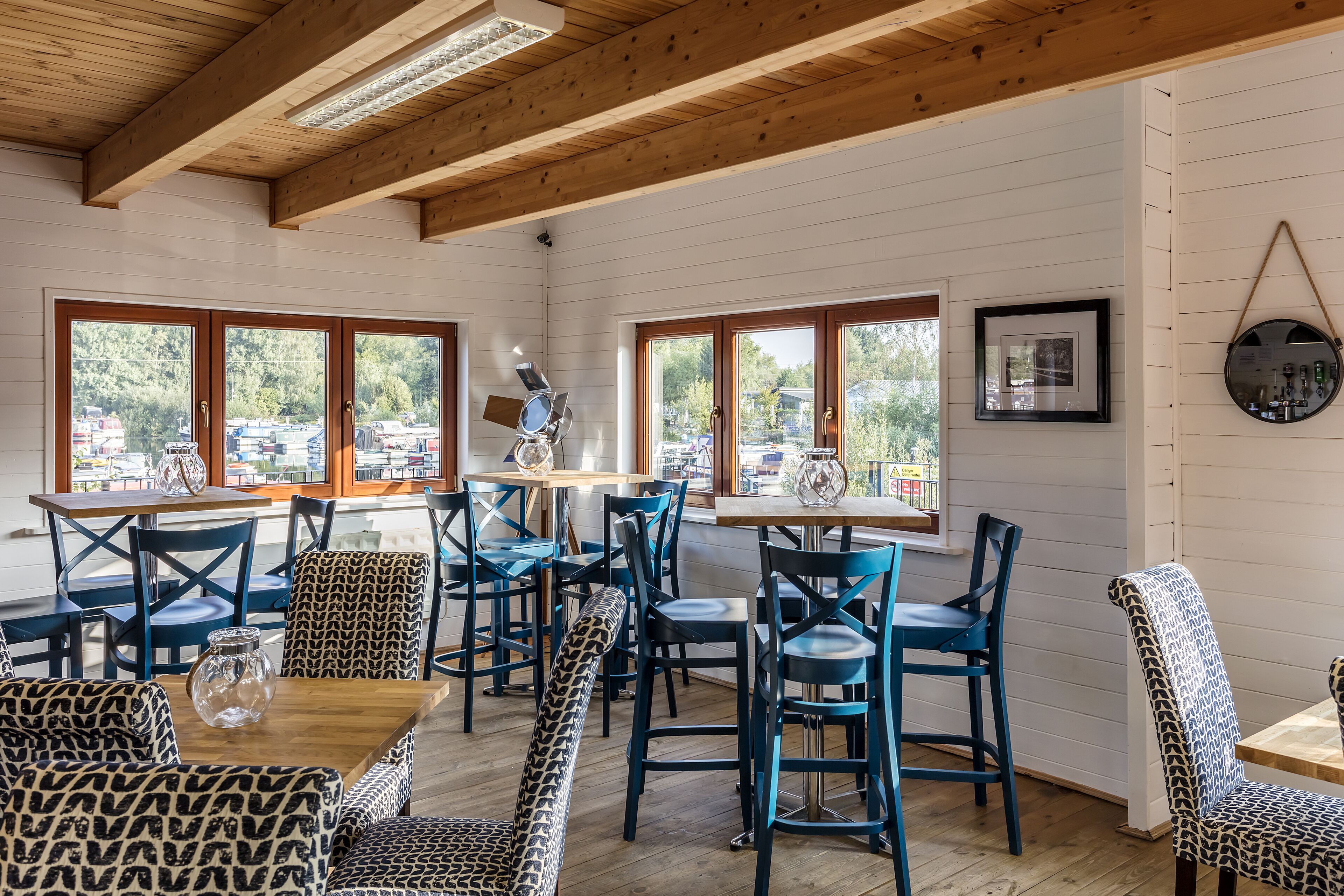 Un comedor con mesas y sillas de madera, ventanas amplias con vistas al exterior y techo de madera.