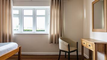 A bedroom with a bed, a chair, a desk, and a window with curtains.