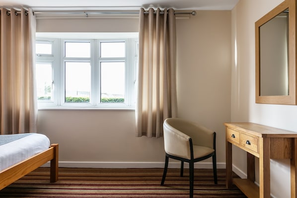 A bedroom with a bed, a chair, a desk, and a window with curtains. - Roydon Marina Village Hotel (Harlow)