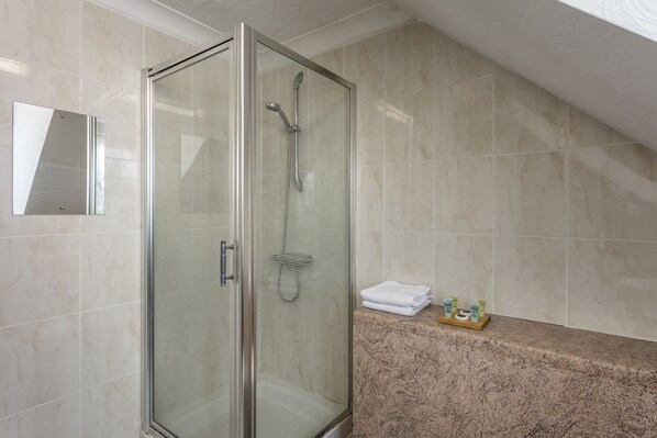 Un box de ducha moderno con puerta de vidrio, pared con azulejos de mármol y encimera de granito con artículos de aseo.