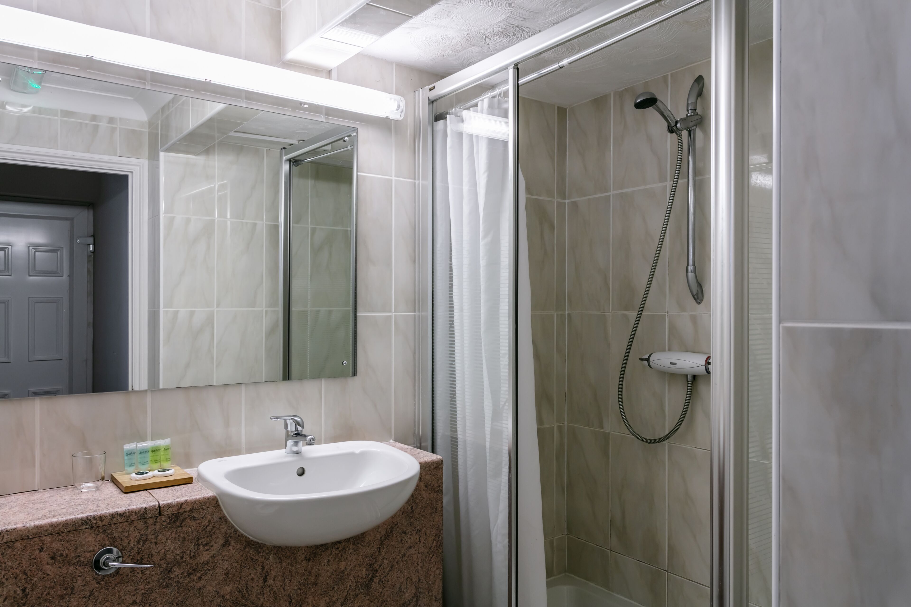 Een badkamer met een witte wastafel, een douchecabine van glas en een spiegel boven de wastafel.