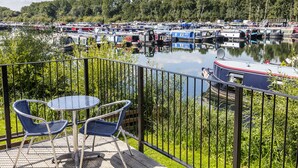 A balcony with two blue chairs and a table overlooking a marina with boats. - Roydon Marina Village Hotel (Harlow)