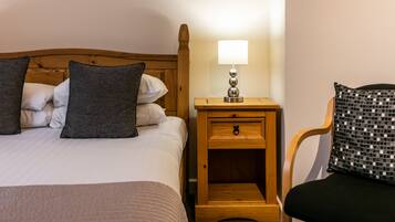 A neatly made bed with pillows, a bedside table with a lamp, and a chair with a patterned cushion.