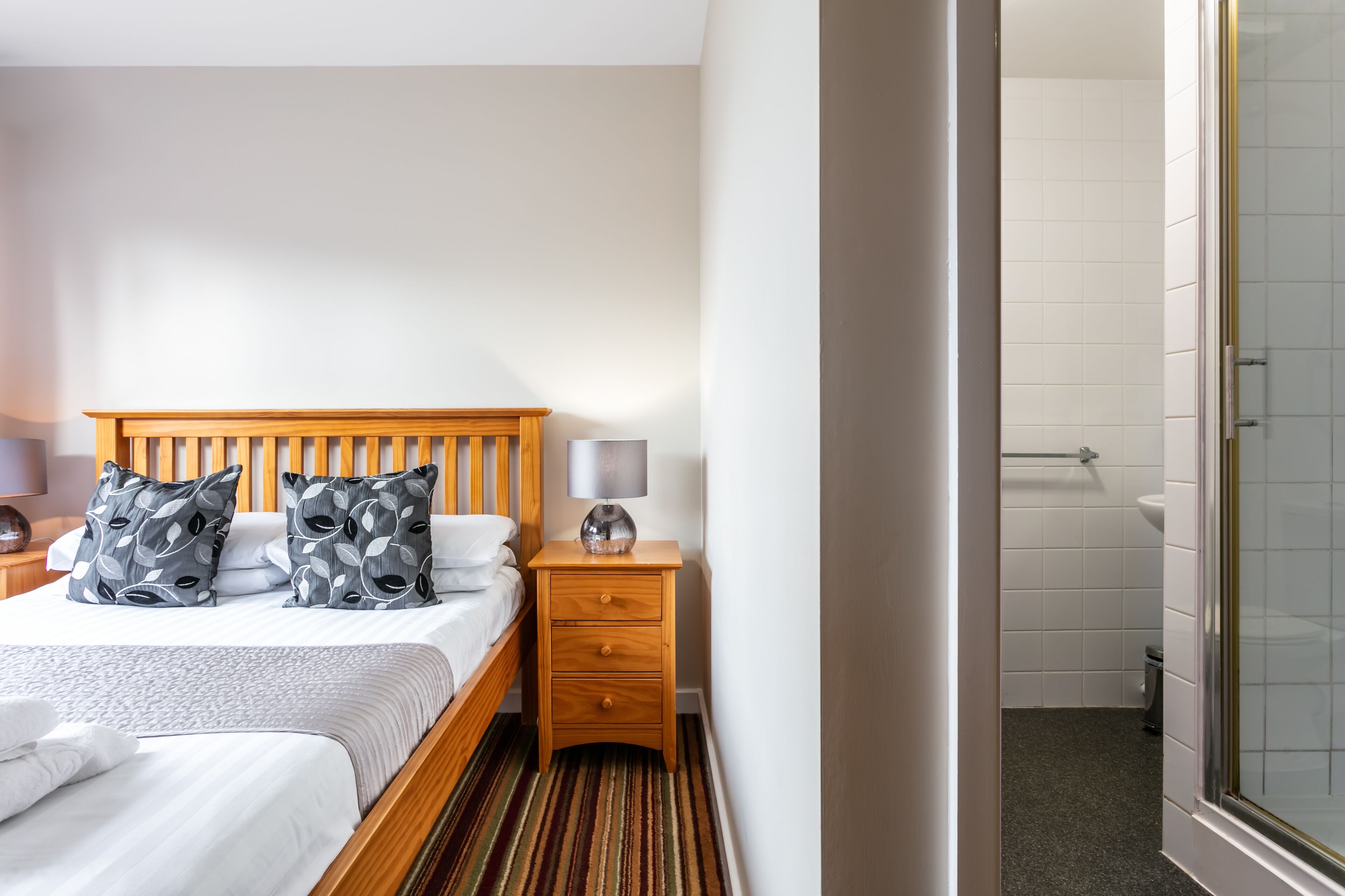 Ein Hotelzimmer mit einem hölzernen Bett, zwei Nachttischen, einer Lampe und Blick ins Badezimmer.