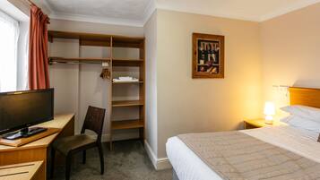 A hotel room with a bed, a desk with a computer, a chair, a wardrobe, and a wall-mounted painting.