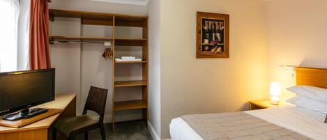 Habitación de hotel con cama, escritorio con computadora, silla, armario y un cuadro colgado en la pared.
