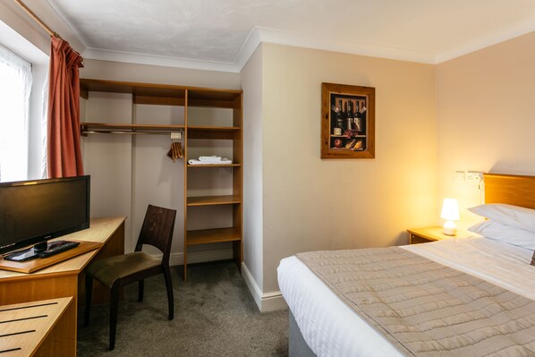 Habitación de hotel con cama, escritorio con computadora, silla, armario y un cuadro colgado en la pared.