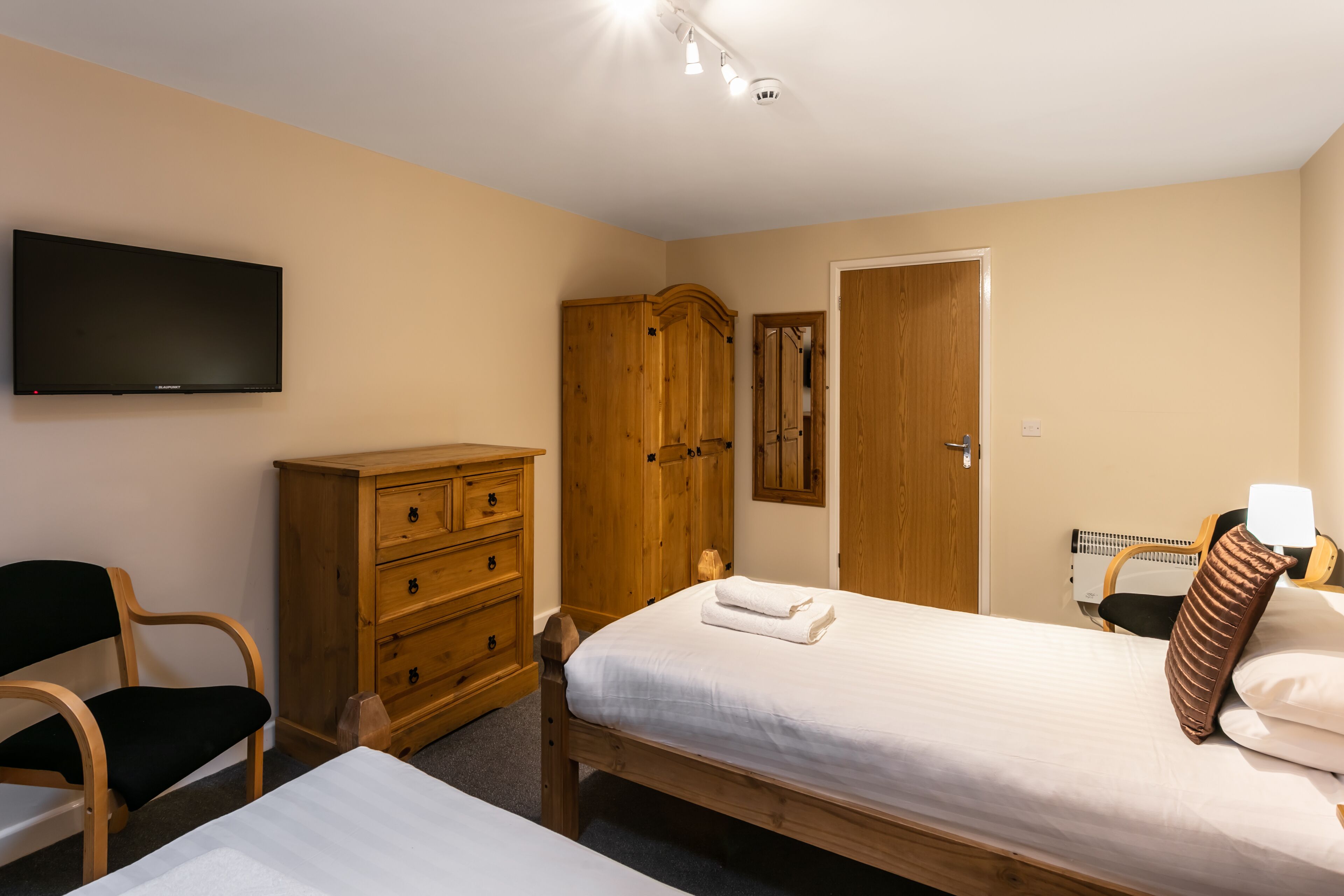 A bedroom with a bed, a wooden dresser, a television, and a door.