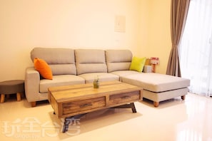Un salon moderne avec un canapé d’angle gris, une table basse en bois et une petite table d’appoint.