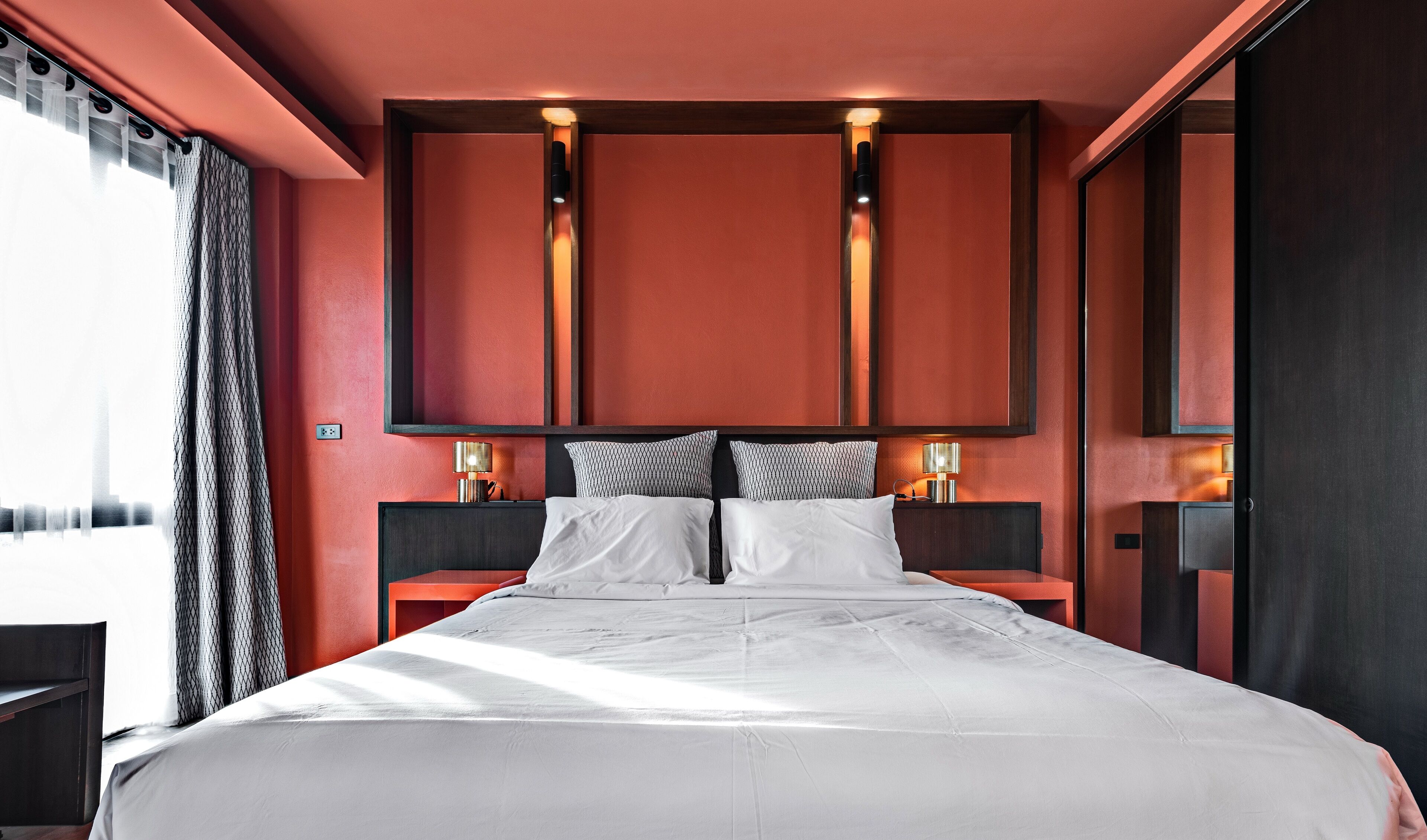 Una habitación de hotel moderna con una cama grande, dos mesitas de noche con lámparas y un espejo grande sobre la cama.