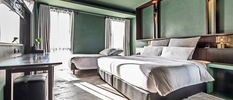 Una habitación de hotel moderna con una cama grande, dos mesitas de noche, un escritorio y una ventana con cortinas.
