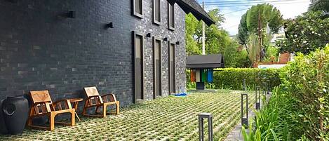 Een modern gebouw met een bakstenen gevel, een kleine tuin met gazon en zitplaatsen, en een klein bouwwerk met een kleurrijke gevel.