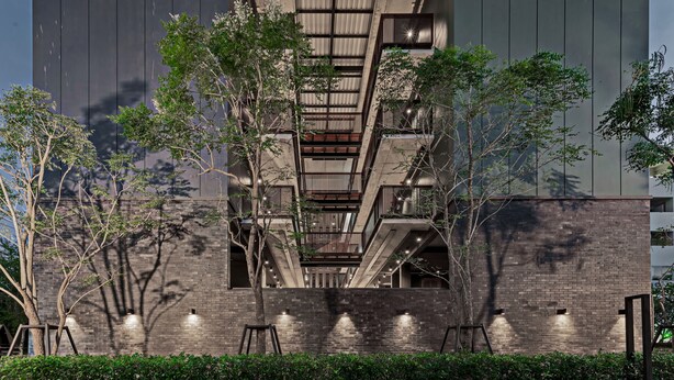 A modern building with a central staircase, surrounded by trees and a brick wall.