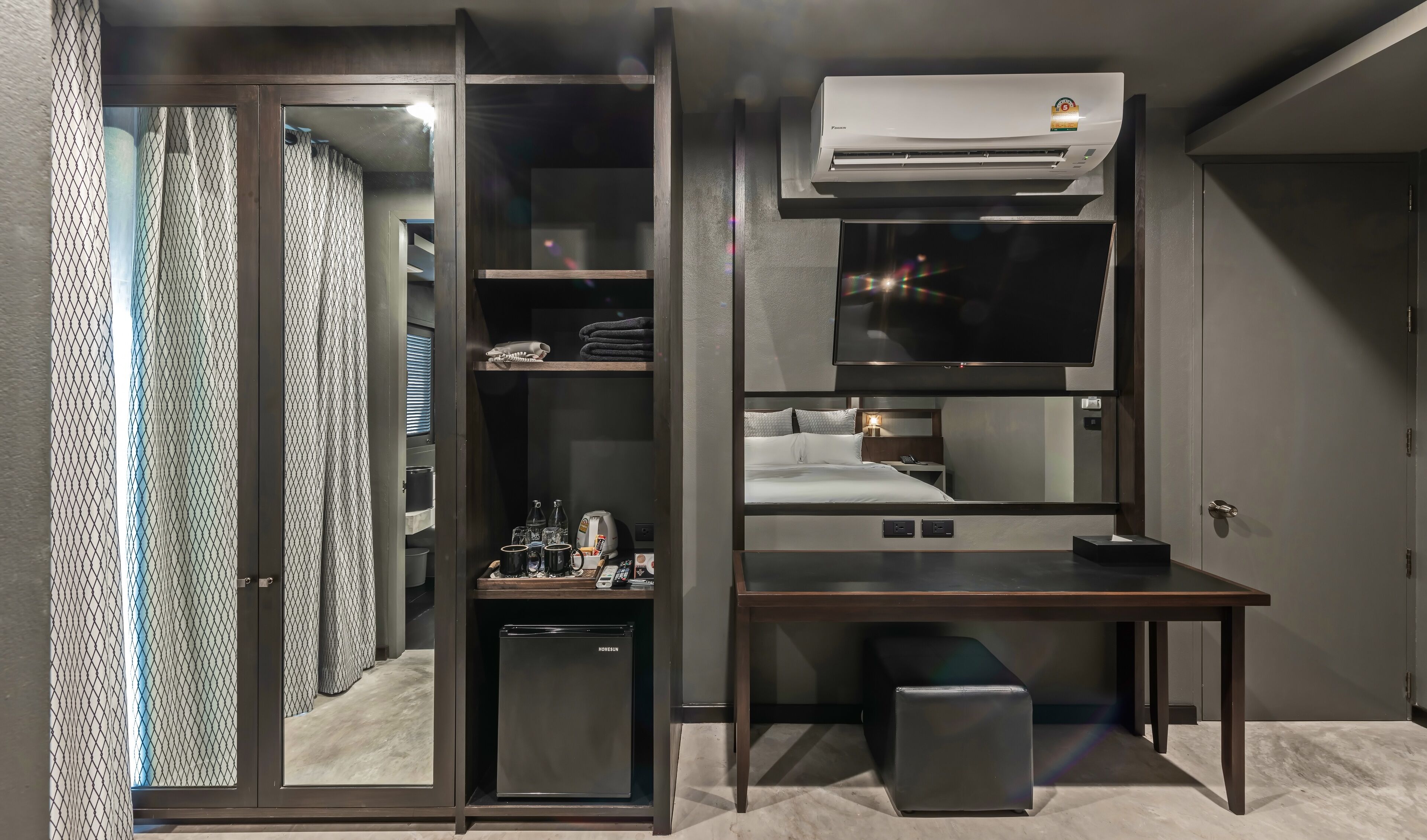 A compact hotel room with a Murphy bed, a small kitchenette, a built-in TV, and a ceiling-mounted air conditioner.