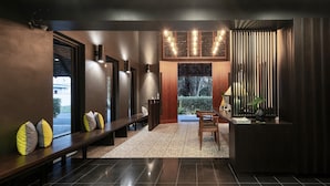 A modern interior with a dark-toned reception desk, a bench with cushions, a patterned rug, and a view through a large window.