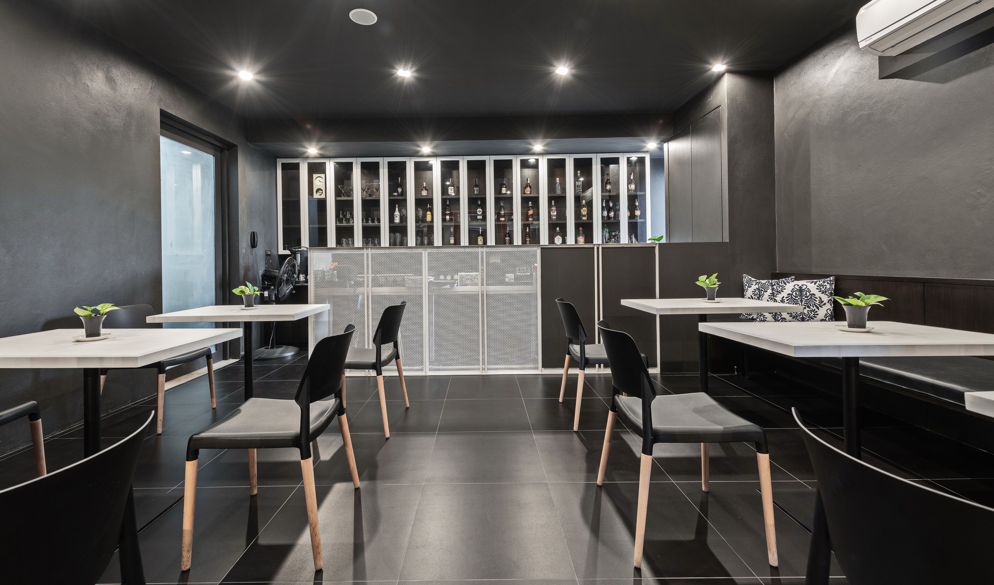 Une pièce moderne, à la lumière tamisée, avec une longue table et des chaises, un appareil à café et un présentoir rempli de bouteilles.