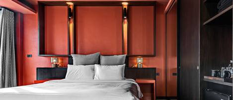 Una habitación de hotel moderna con una cama grande, dos mesitas de noche con lámparas, un armario y un minibar.