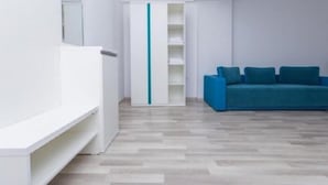 Ett modernt, minimalistiskt rum med en blå soffa, vita hyllor och ett ljust trägolv.