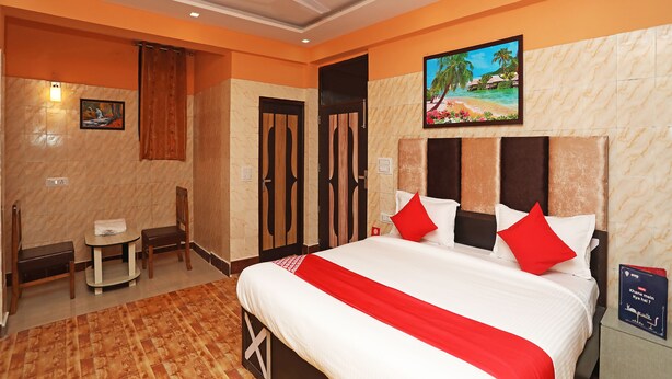 A hotel room with a large bed, a ceiling fan, a painting of a beach scene, and a small table with a chair.