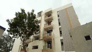 A multi-story building with balconies, a tree in the courtyard, and a brick pathway.