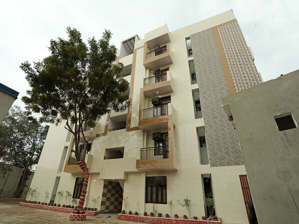 Un edificio de varios pisos con balcones, un árbol en el patio y un camino de ladrillo.
