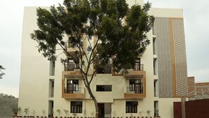 A multi-story building with balconies, a tree in front, and a patterned wall on the right.
