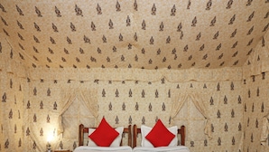 A double bed with a red and white bedspread, two red pillows, and a wooden headboard. The room has patterned wallpaper and a nightstand with a lamp. - OYO 28028 Rishikul Sangam City (Karchana)