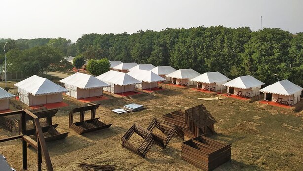 A series of white tents arranged in rows on a grassy field with a forested hill in the background. - OYO 28028 Rishikul Sangam City (Karchana)