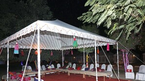 A tent with white walls and a patterned roof, furnished with white chairs and red carpets. - OYO 28028 Rishikul Sangam City (Karchana)