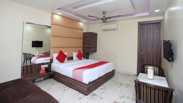 A modern hotel room with a large bed, a ceiling fan, a TV, and a wooden wardrobe. - OYO 27864 Hotel Samrat (Gurugram)
