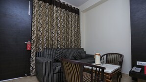 A room with a striped sofa, a dining table with chairs, a telephone, and a wall with a wavy pattern. - OYO 27864 Hotel Samrat (Gurugram)