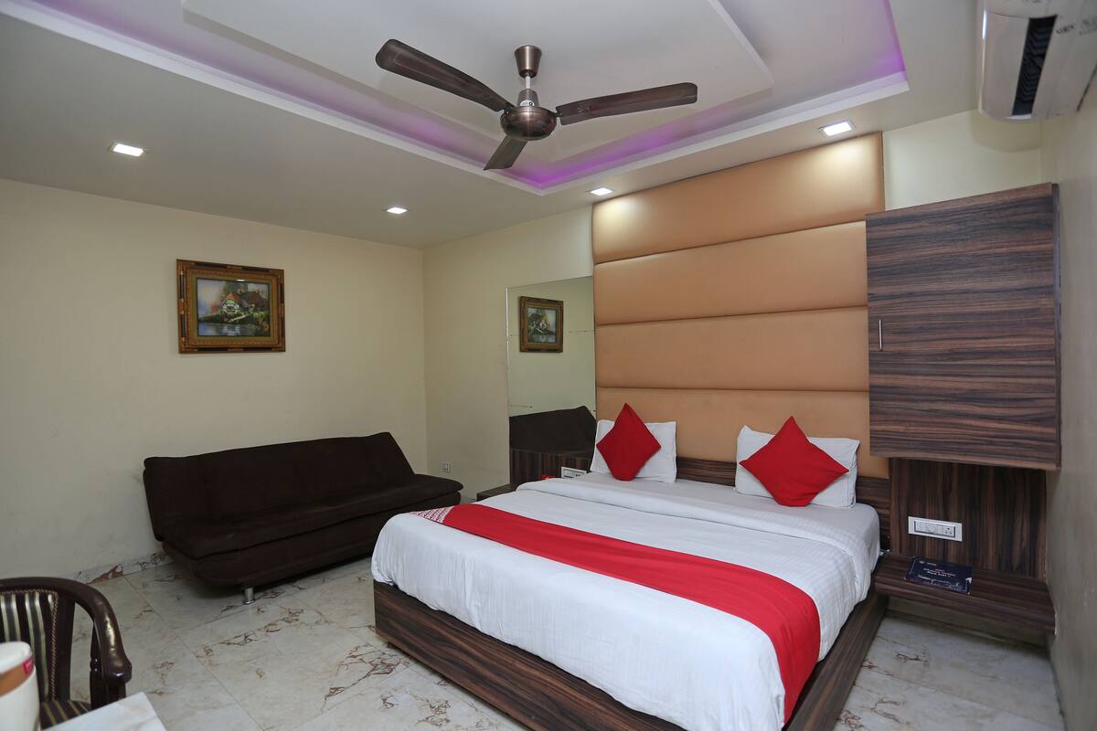 A hotel room with a bed, a ceiling fan, a dark-colored sofa, and a wooden wardrobe.