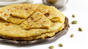 A round, golden-brown flatbread on a metal plate with a cup and saucer in the background. - OYO 27864 Hotel Samrat (Gurugram)