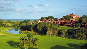 A golf course with a pond, palm trees, and a view of the ocean. - San Lameer Villa  Rentals 2507 (Southbroom)