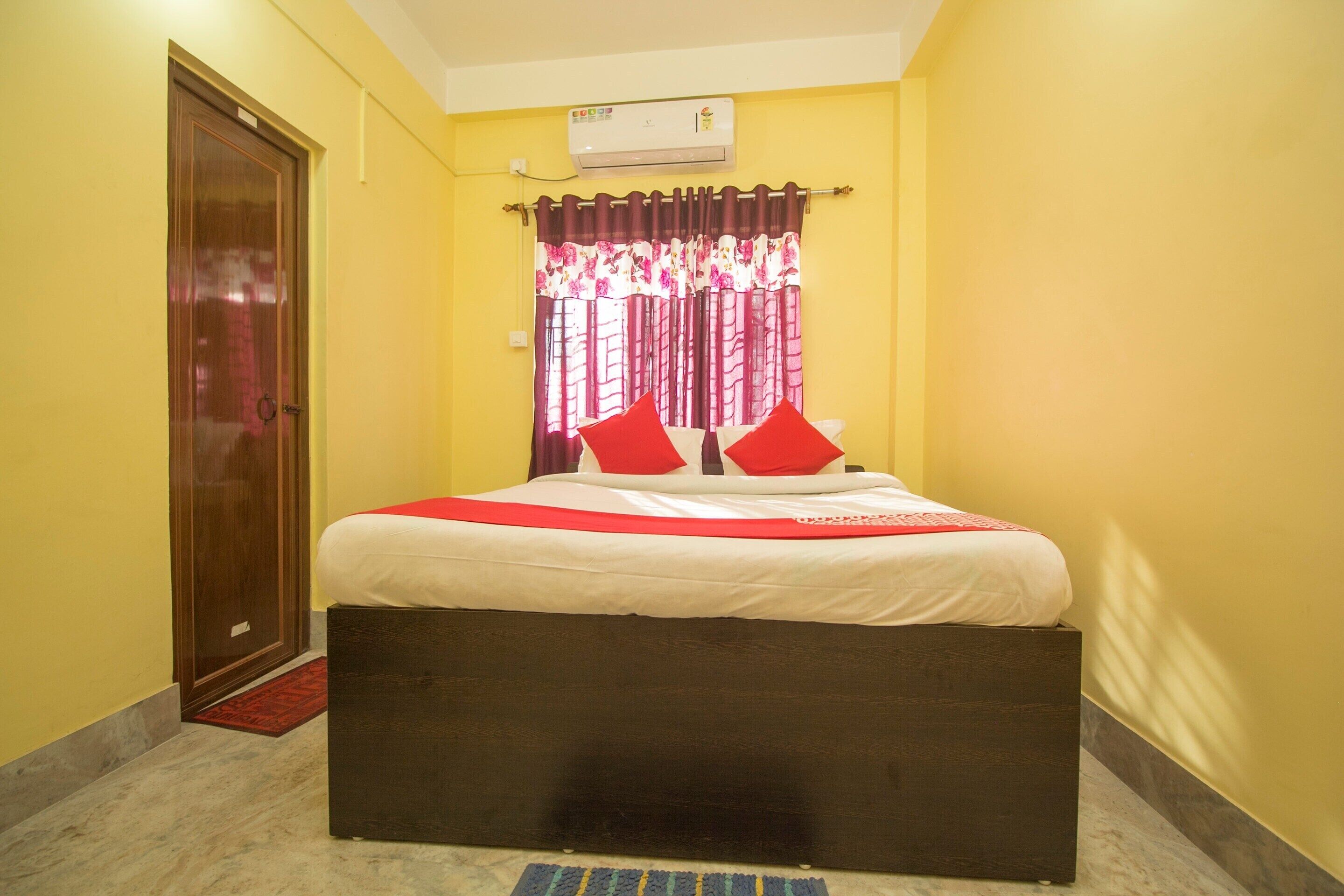 A bedroom with a bed, a wooden door, a red and white curtain, and an air conditioning unit.