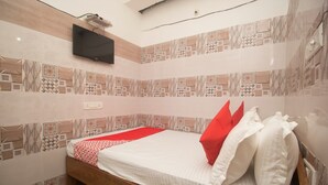 A neatly made bed with a red and white bedspread, a wooden headboard, and a wall-mounted TV.