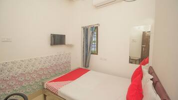 Un dormitorio con cama, televisor, ventana con cortinas y espejo.