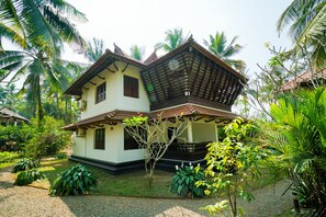 A two-story house with a balcony, surrounded by lush greenery and palm trees.